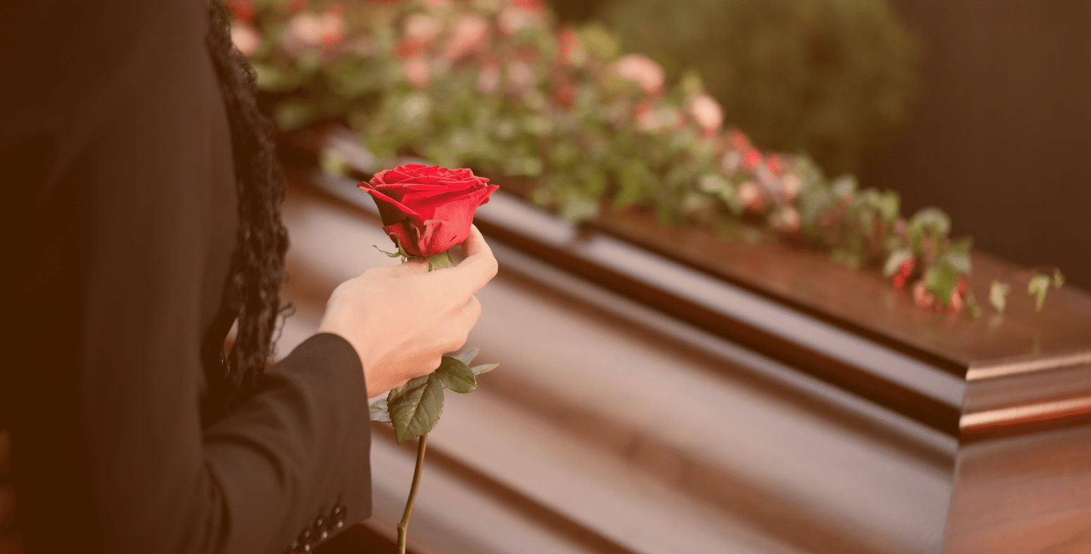 Osoba stojąca z różą przy trumnie na pogrzebie