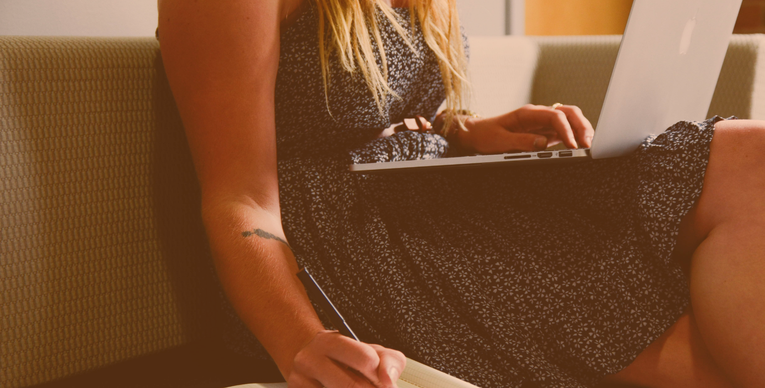 kobieta z laptopem na kolanach rozpisująca zadania na kartce papieru