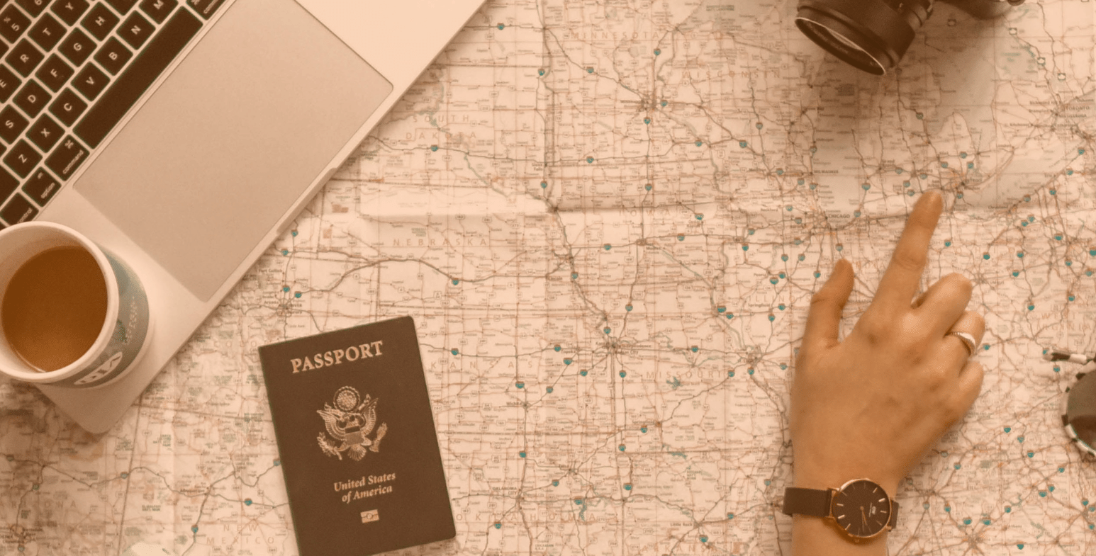Rozłożona mapa, na której leży laptop oraz paszport. Osoba wskazuje dłonią lokalizację.