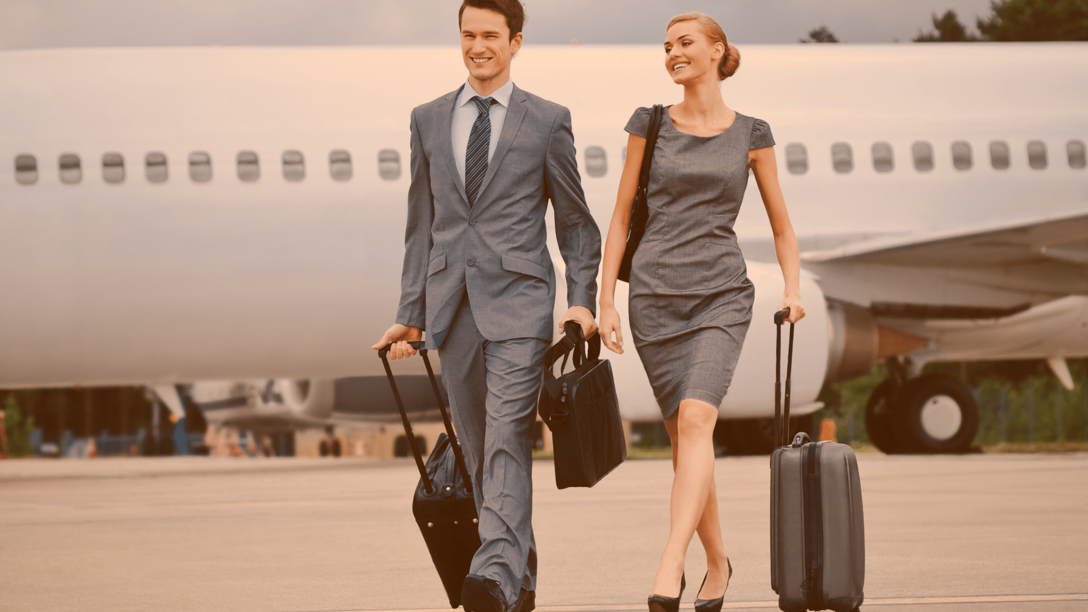 Formalnie ubrani kobieta i mężczyzna odchodzą z walizkami od samolotu.